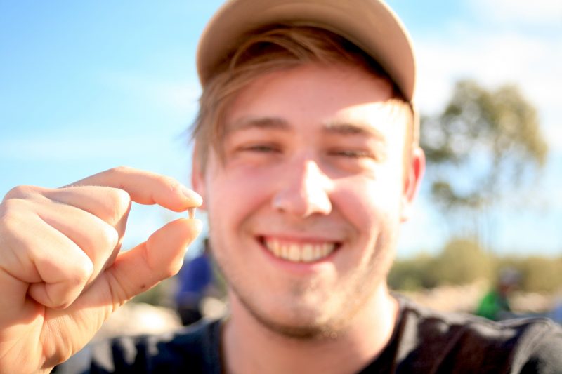 Smiling young man outdoors in sunny rural setting, holding up a small tooth