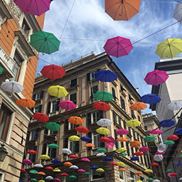 Artistic public display of colourful umbrellas suspended in the sky among city buildings