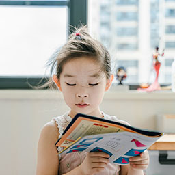 a young Asian girl reading a book in a classroom setting