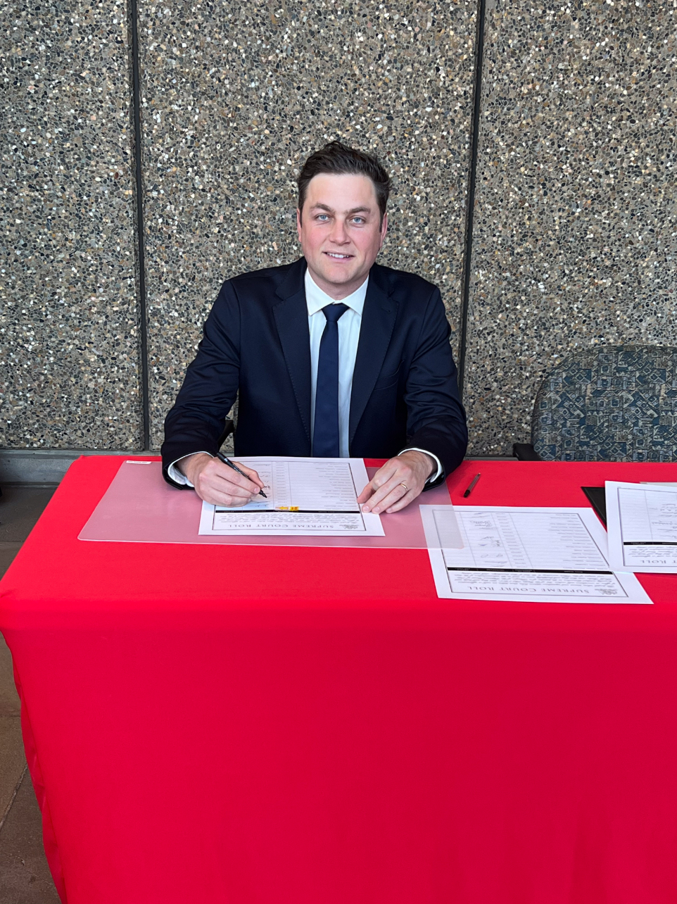 Man sitting at desk with red table clith signs official documents