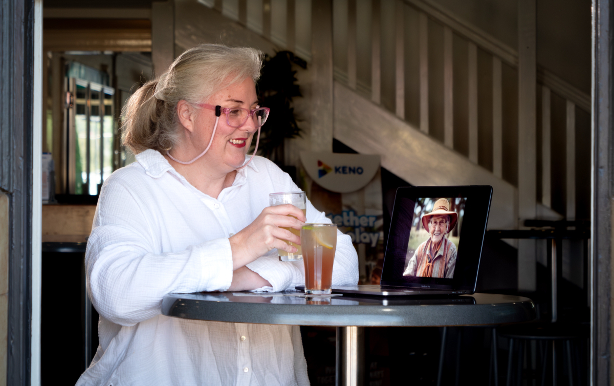 Woman at a pub table looks at laptop computer screen carrying an AI-generated image of an older woman.