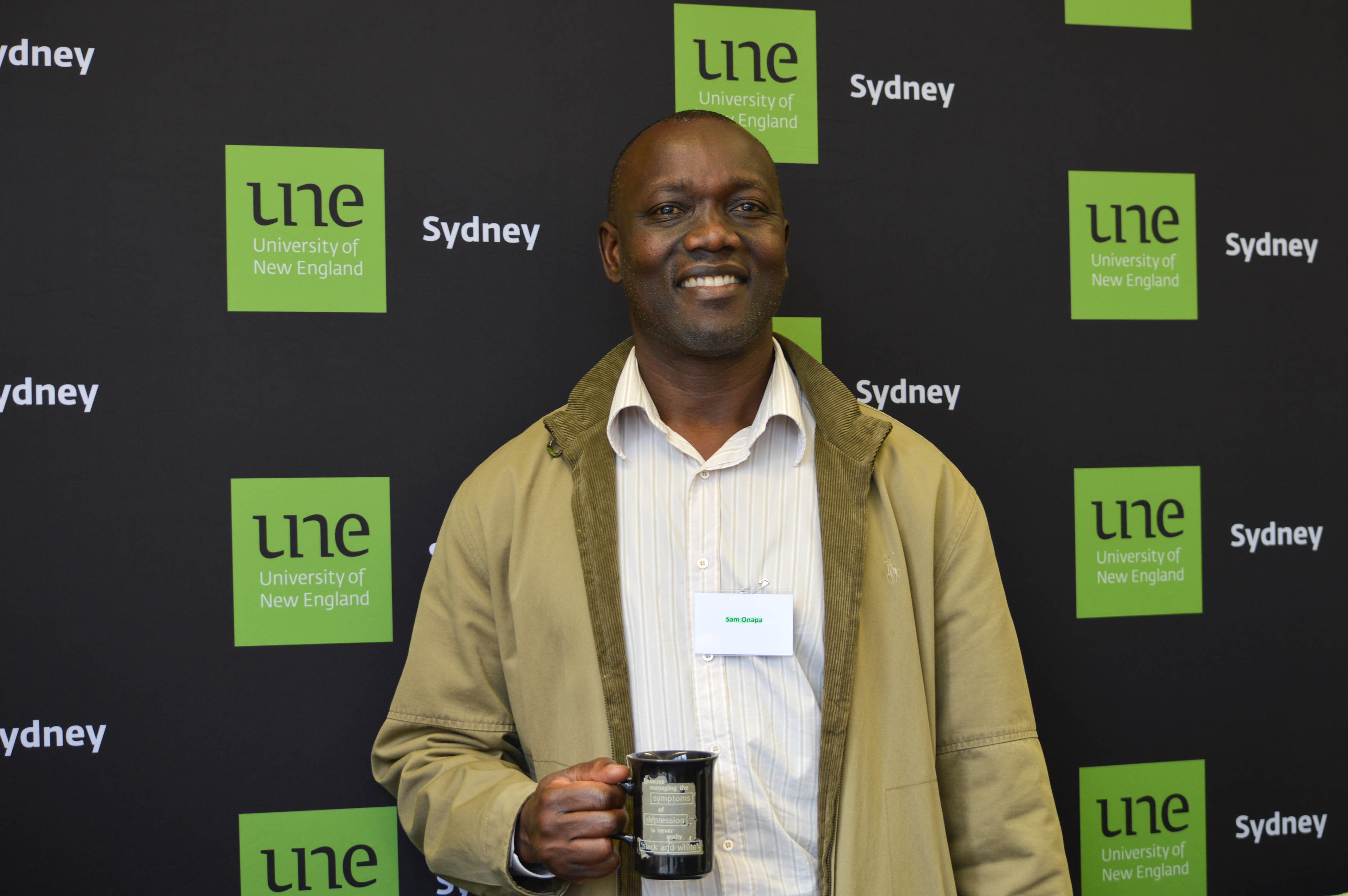 Sam Onapa standing in front of a UNE Sydney banner