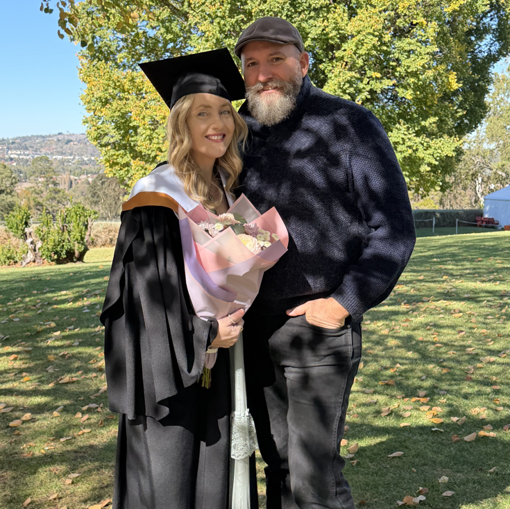 Rebecca in her graduation robe standing with her husband  on her graduation day