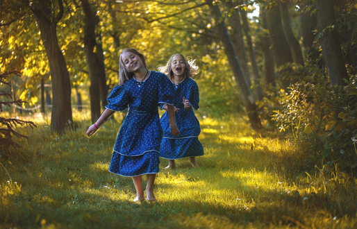 Two small twin girls in blue dresses playing in the forest facing frontwards to camera 