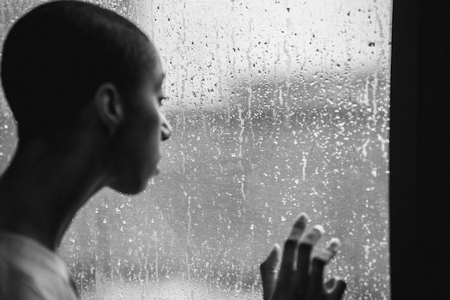 Man looking out of rainy window with hand against window