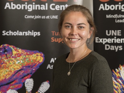 Indigenous UNE student in white button-down shirt smiles in conversation with an out-of-sight person