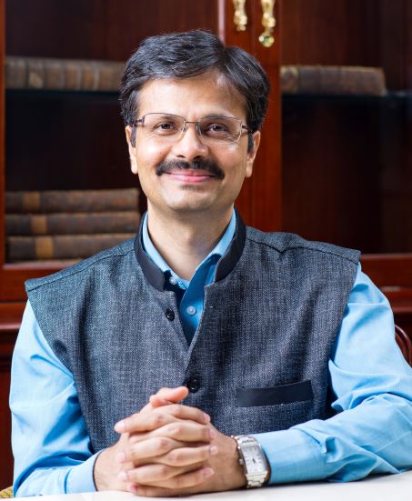 A portrait photo of Professor Surya Deva with bookshelves in the background