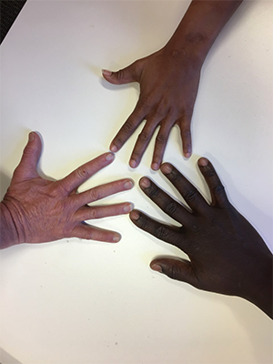 Birds-eye perspective of three human hands in three skin tones touching at the fingertips