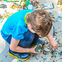 Young boy in blur shirt crouched over small pieces of a mechanical toy car building set 