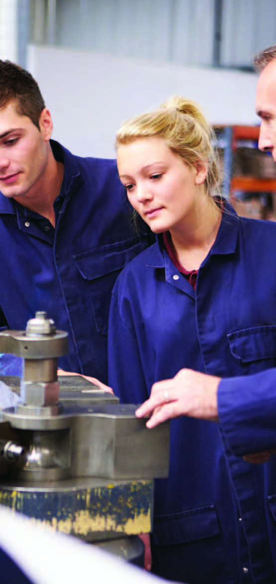 Image of some people wearing blue boilersuits looking with interest at a piece of  machinery