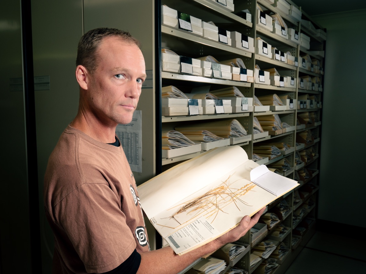 Boyd Wright holding a plant collection folio displaying a dried specimen of spinifex.