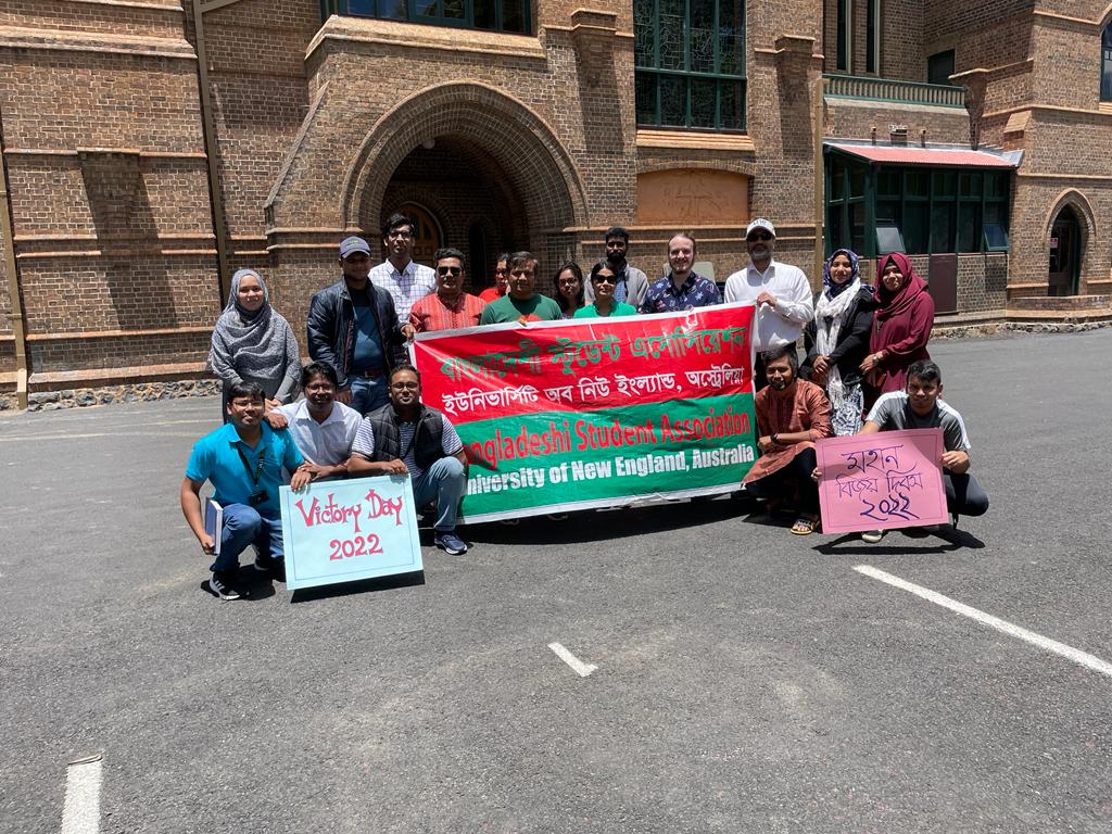  Bangladeshi Students Association of UNE community program post for photo with a large banner at carpark 