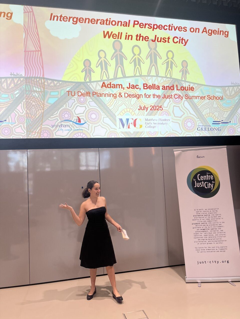 A teenaged Bella presenting wit ha PowerPoint presentation on stage.