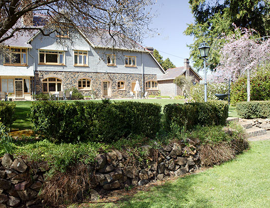 Three-storey shingle house and front garden with ivy hedges and stone retaining wall 