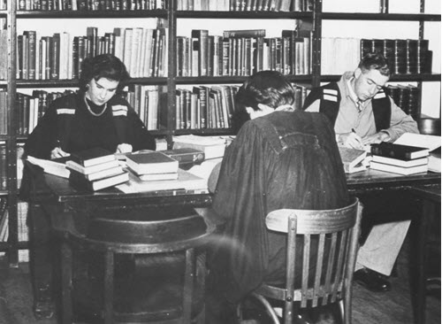 Dixson Library in the early days with 3 students studying at a desk in their academic dress.