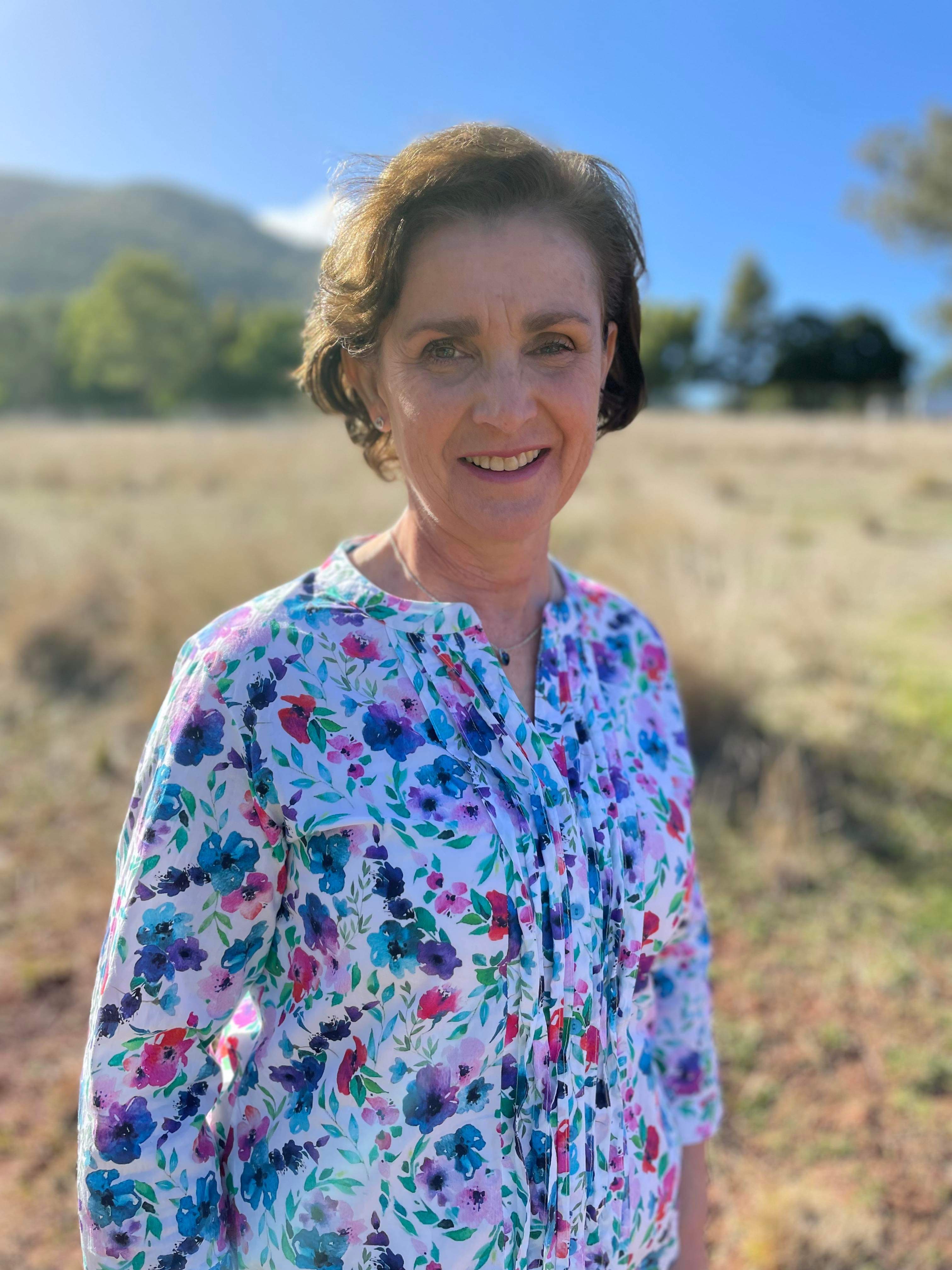 Mature female student standing in a field wearing a white floral shirt.
