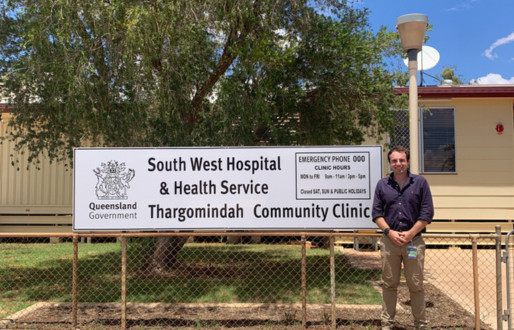 Man in pant and shirt stands in front of medical clinic sign in remote Queensland.