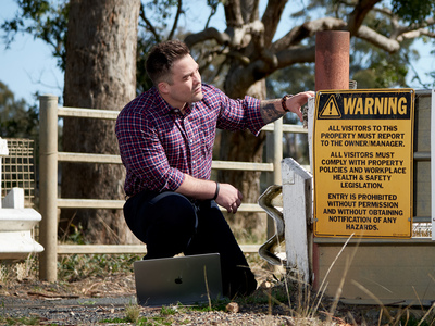 UNE student crouches in outdoor setting next to hazard sign
