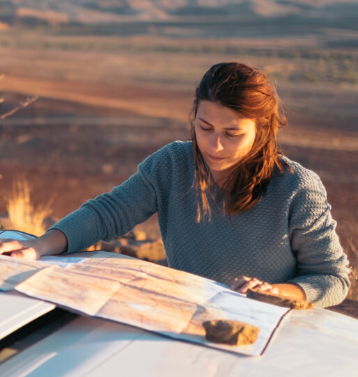 A woman resting a map on the hood of her car. 