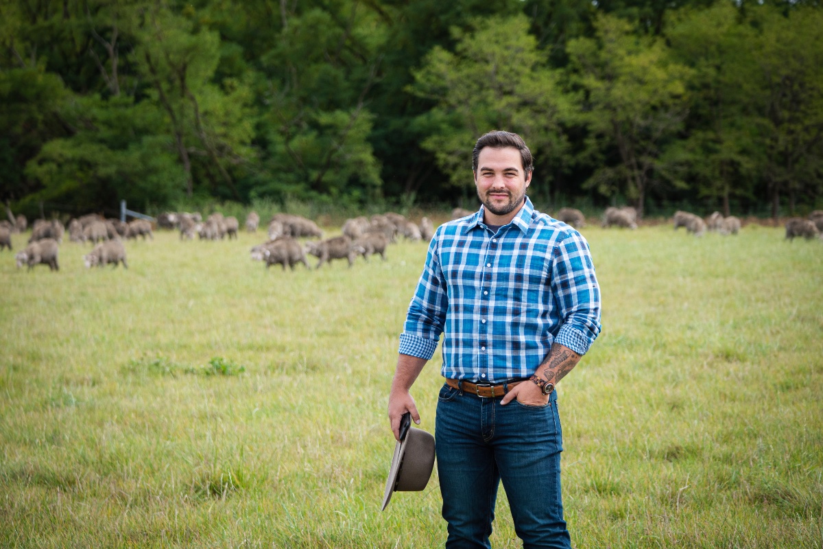 Dr Kyle Mulrooney in a paddock with sheep in the background