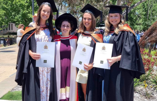Four women in graduation gowns, three are holding testamurs