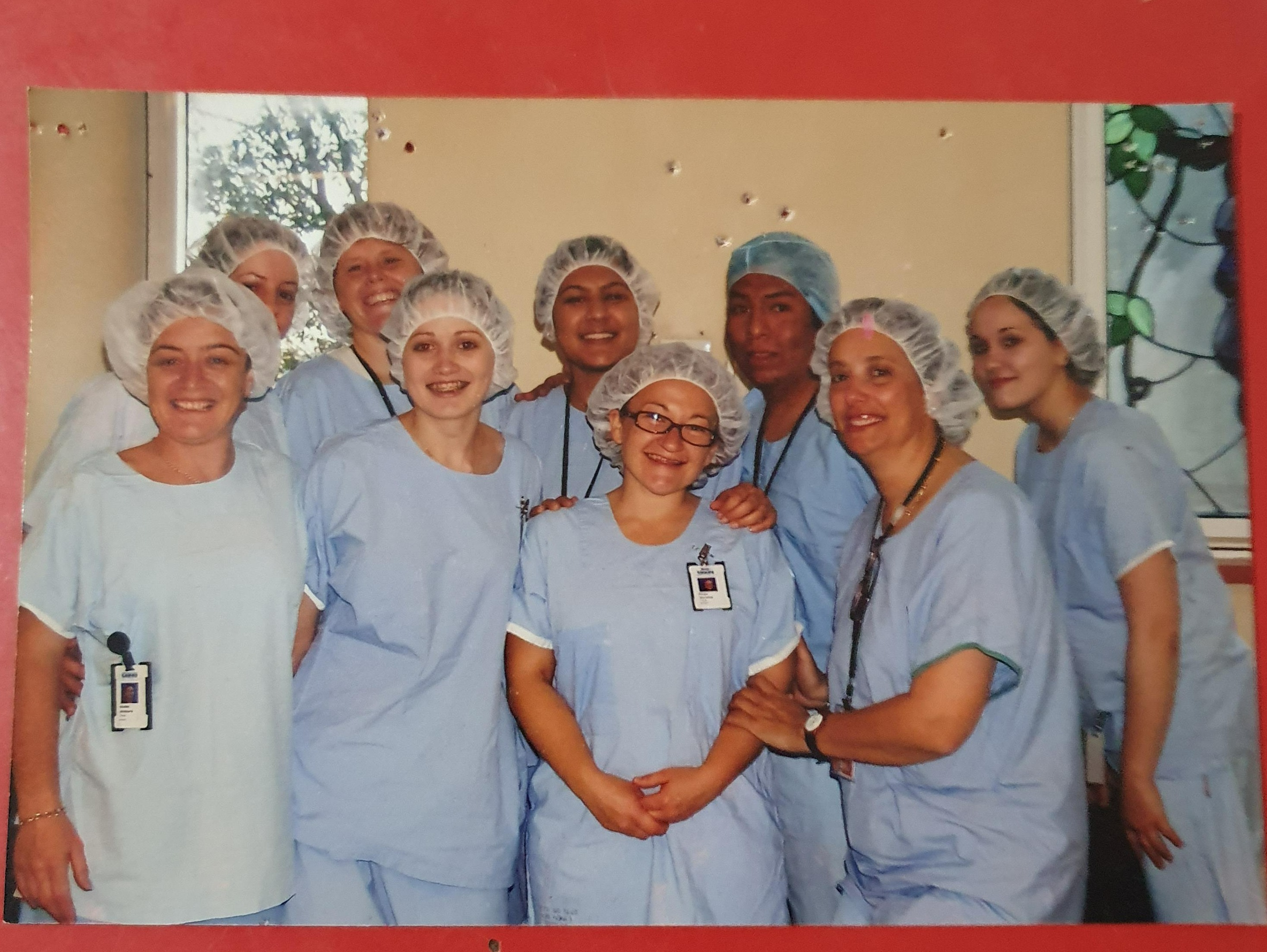 Group photo of nine people in light blue theatre scrubs and hair theatre scrubs and hair nets, standing close together and smiling in two rows.