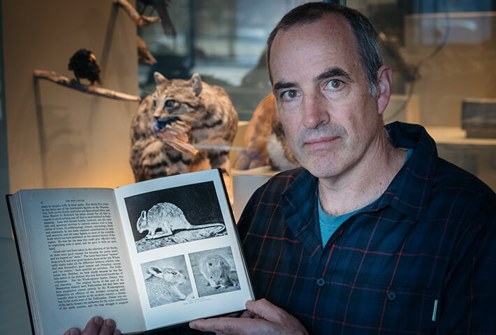 Karl Vernes holding an open book showing photos of the desert rat-kangaroo