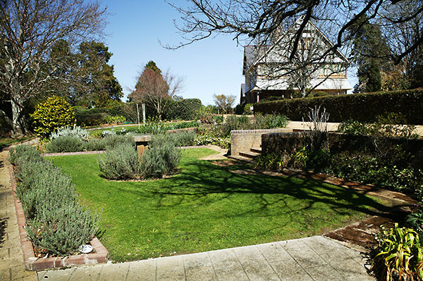 The gardens of Trevenna Homestead, showing stone paths and lavendar plants, with main house in background 