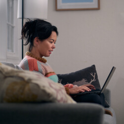 A female student sitting on her couch, feeling relaxed and reading her laptop. 