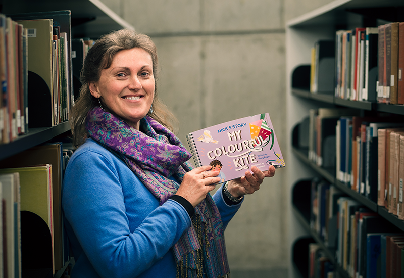 UNe education researcher Dr Marg Rogers in the library holding a bound copy of her children's book My Colourful Kite: Nick's Story