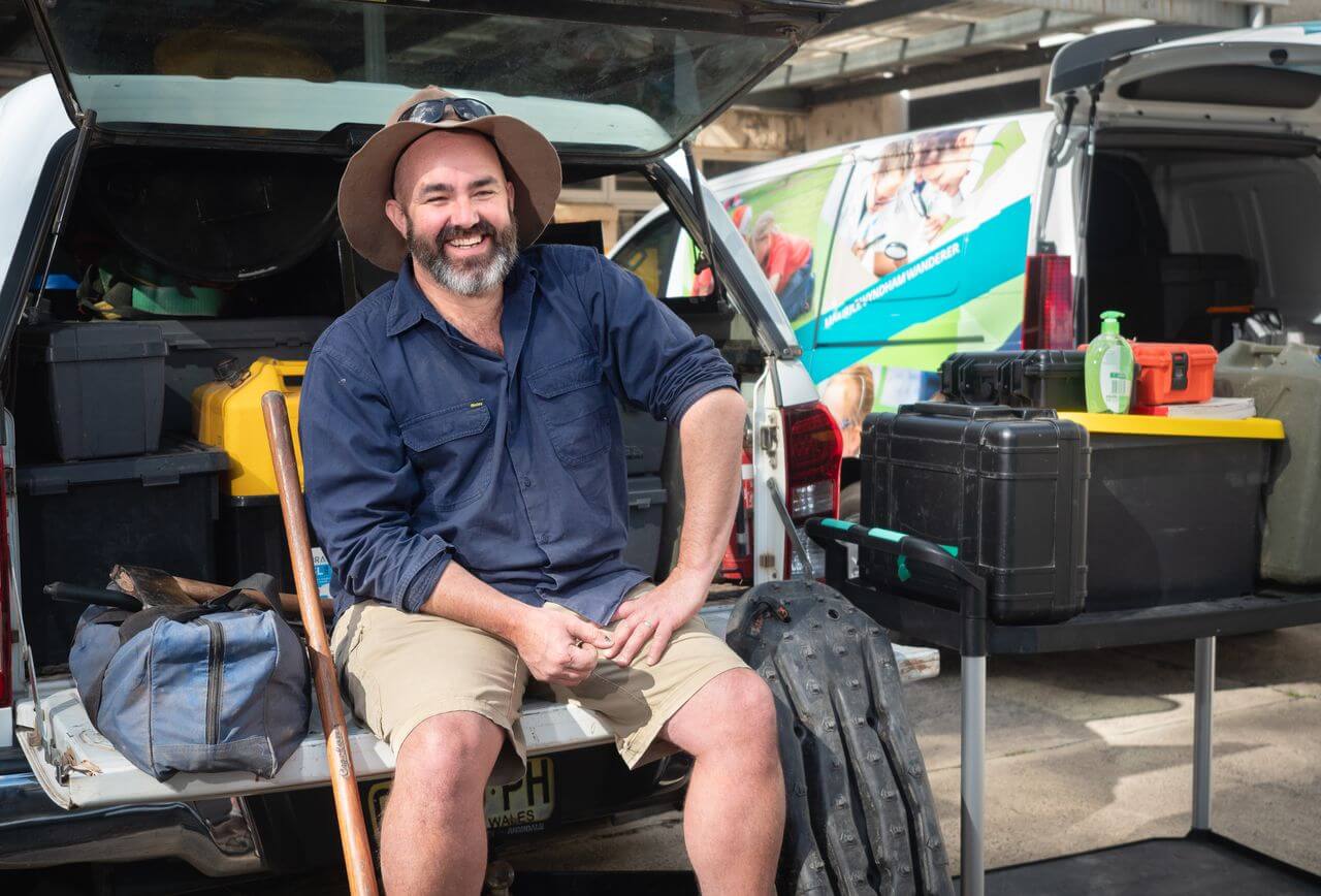 Man sitting on tailgate smiling at camera.