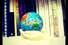 A hand holds a globe with books on a shelf in the background
