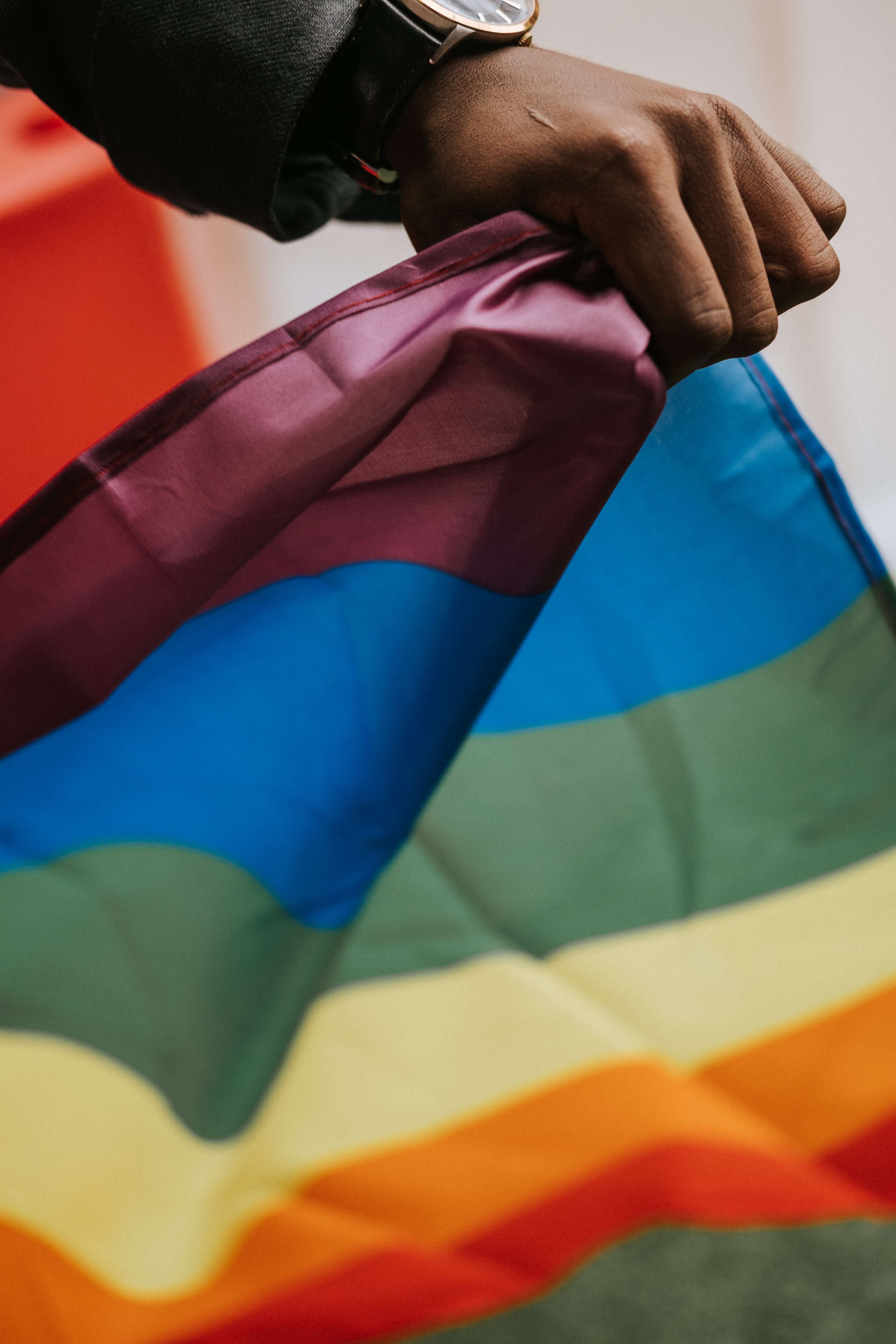 Hand holding the LGBTQIA+ rainbow flag