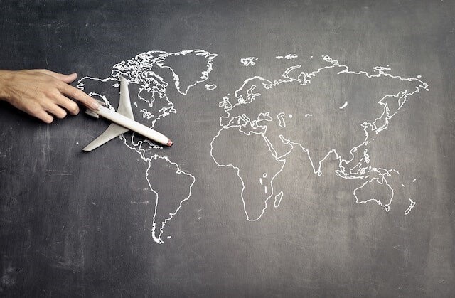 Map of World on a chalk board with hand guiding a toy airplane in top left hand corner