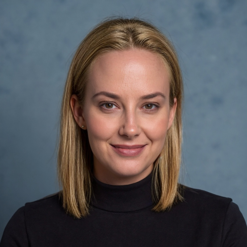 Professional headshot of a woman with straight blonde hair in a black top, smiling slightly against a blue backdrop.