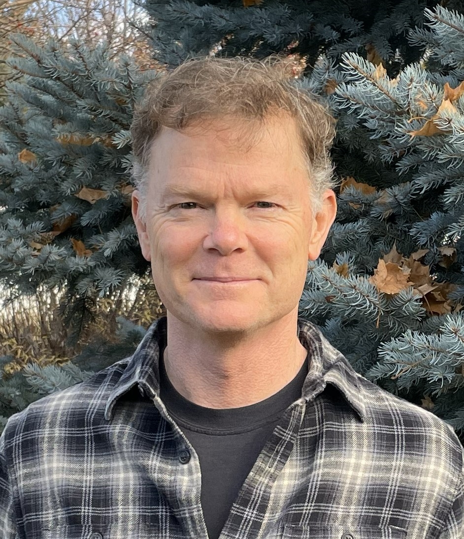 man looks at camera with vegetation in background