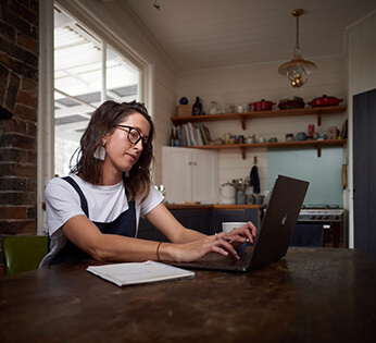 An online student typing on a laptop in their kitchen.