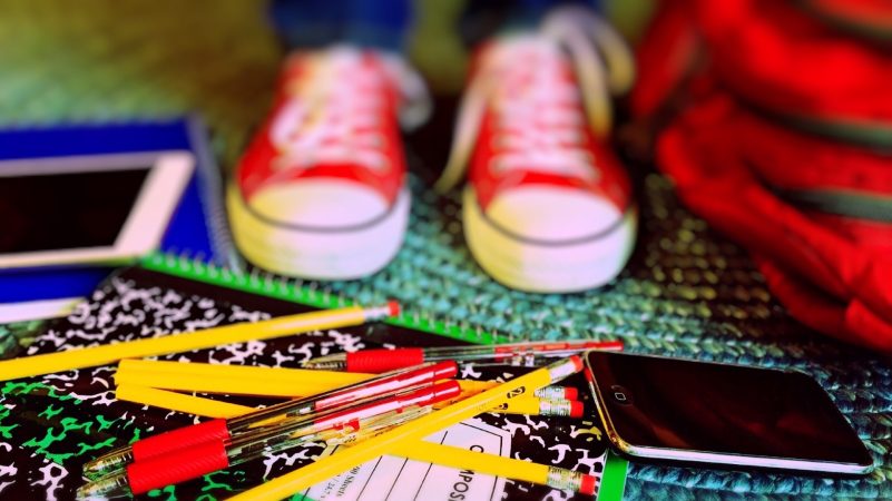 Pens, pencils, books and smartphone on the floor in front of sneakers and school bag