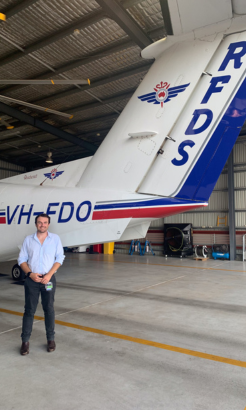 Main poses next to small plane in airport hangar. 