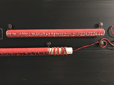 Two pencil-like devices with tightly wrapped red leather twine with lettering 