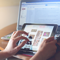 Close-up of hands manipulating images on a tablet with a desktop computer blurred in the background
