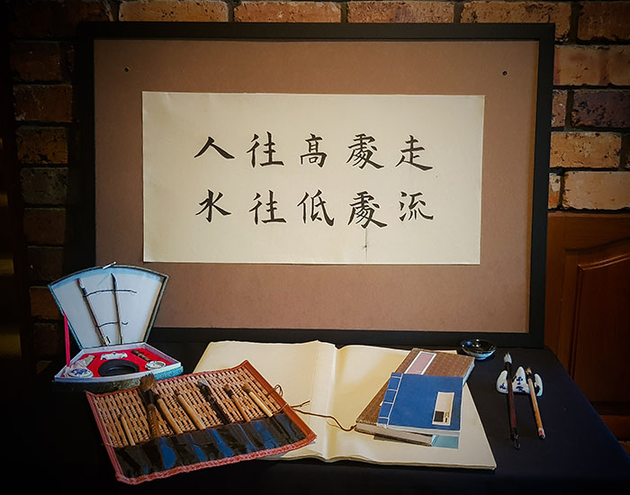 Scroll mounted on natural board with Chinese characters and the tools of the trade are visible as part of the artwork
