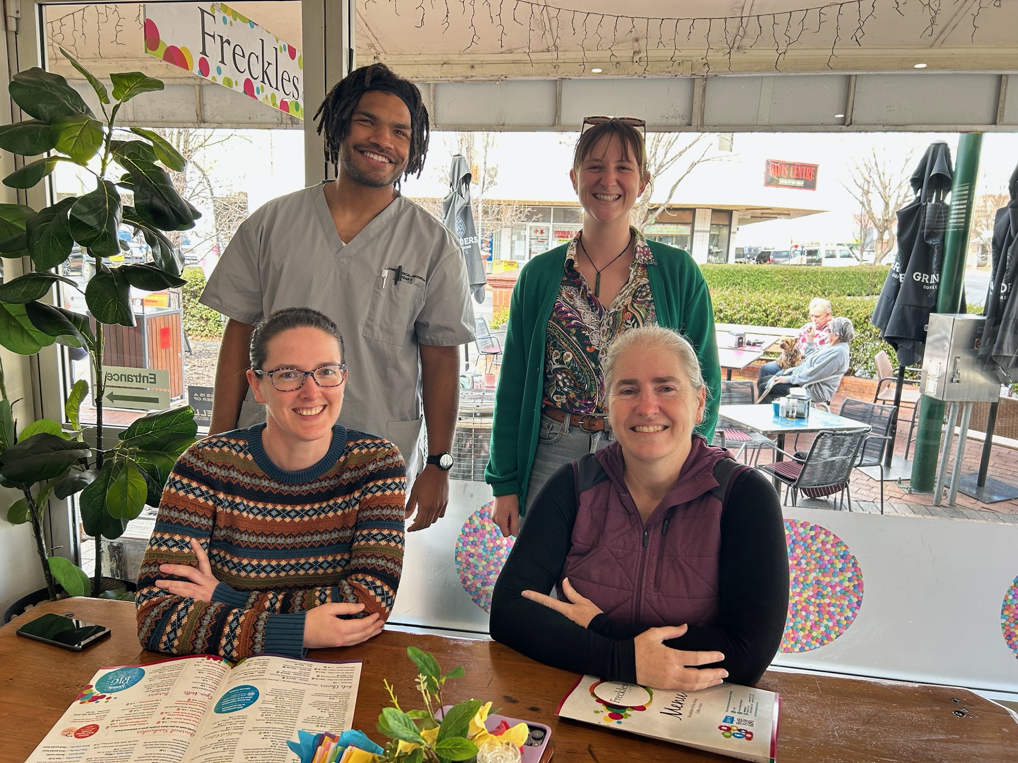 Male medical student in scrubs poses for photo with his three female medical supervisors at a cafe