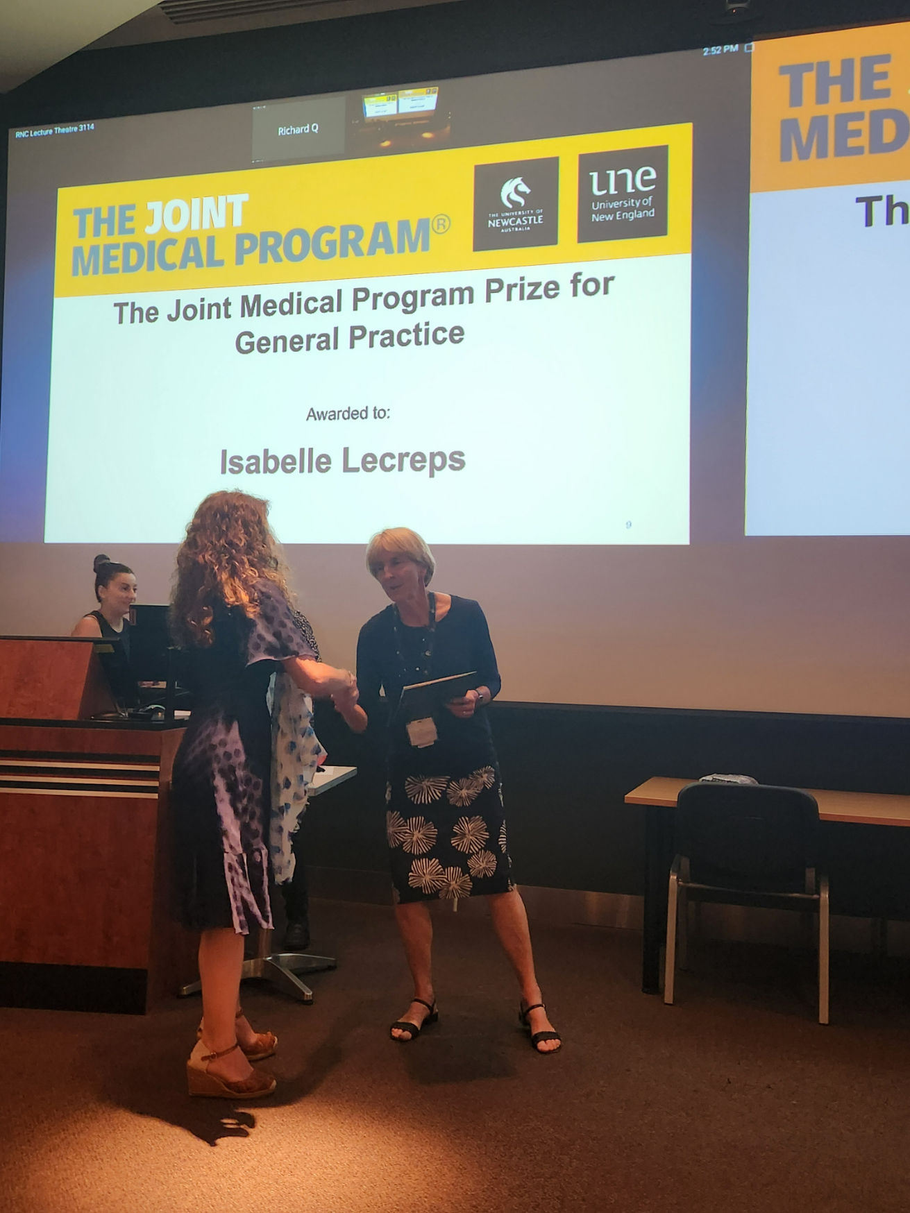 Lady accepting an award from another lady underneath a projector.