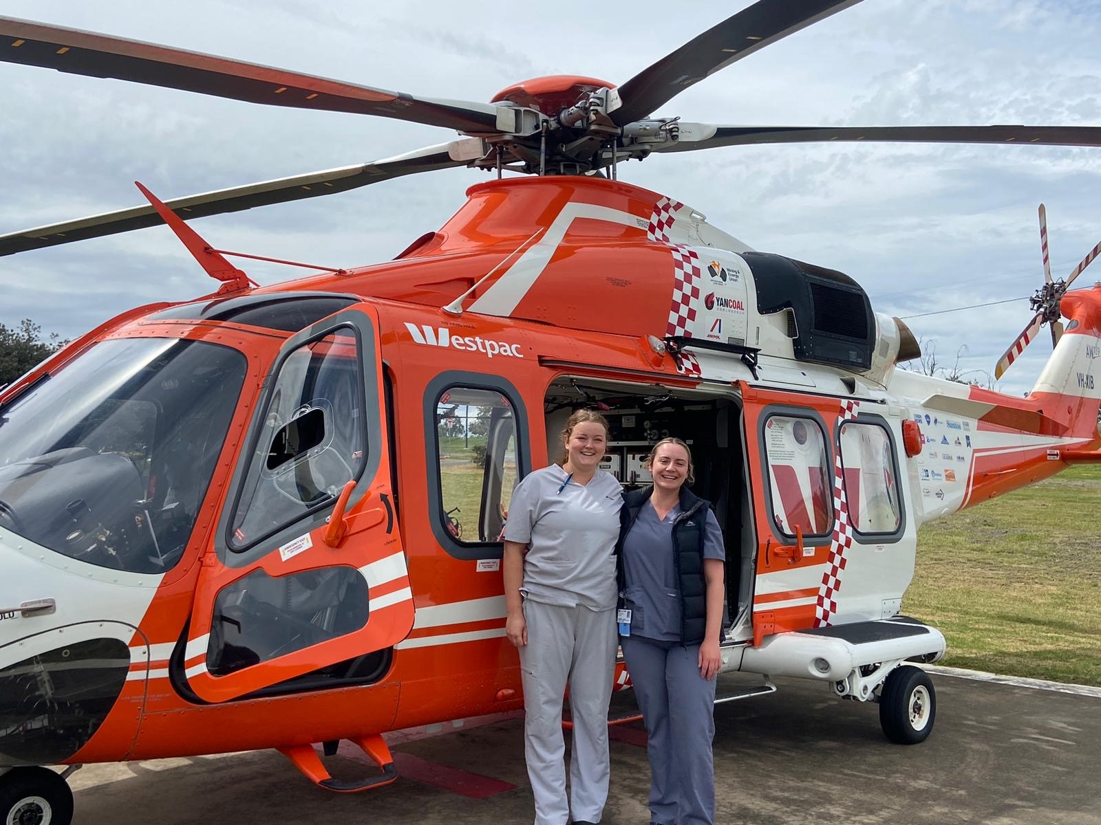 Two young female med student pose for a photo in front of a medical helicopter