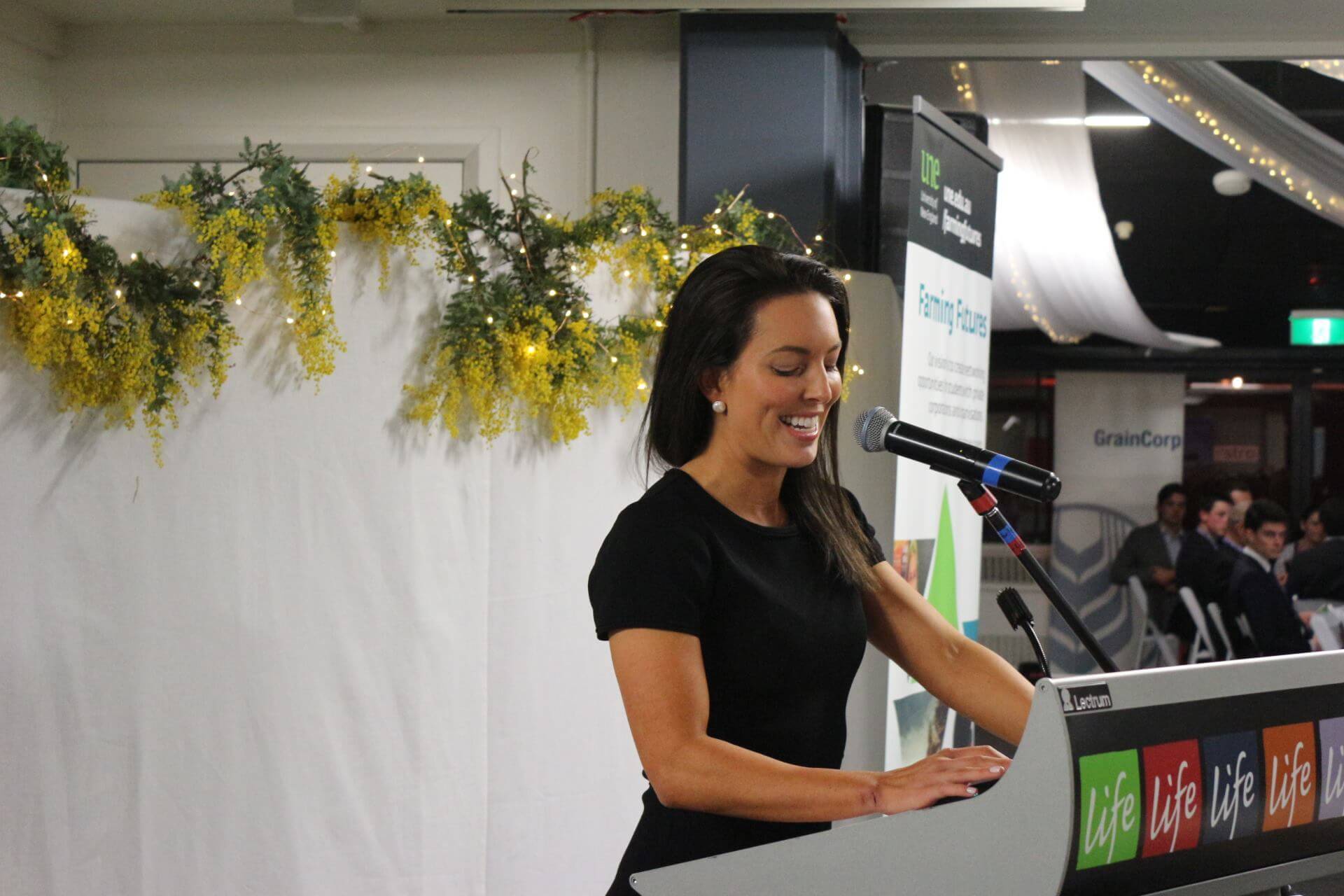 Female guest speaker stands at podium in front of dinner crowd