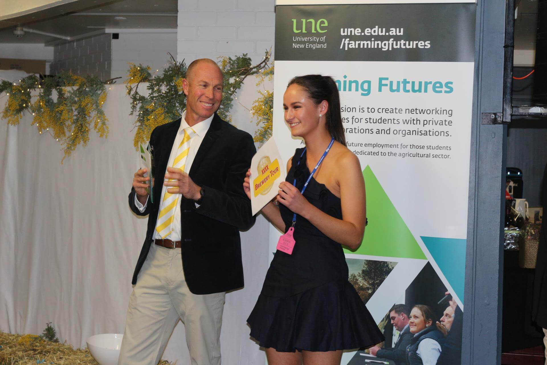 Male auctioneer is auctioning off item and female student holds current item of auction up for crowd to see 