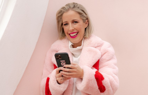 Fashionable woman wearing a big fuzzy coast looks from her phone with a big smile