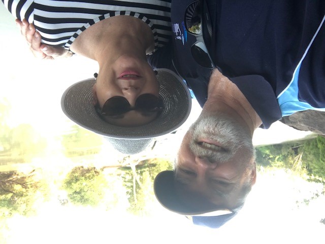 Portrait of older couple with man wearing cap and woman wearing hat and sunglasses, both are smiling