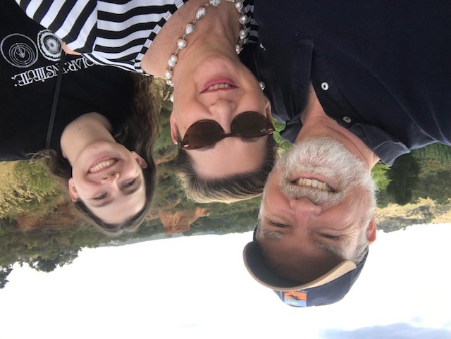 Older couple on holiday facing portrait to camera smiling with teenage daughter smiling in background